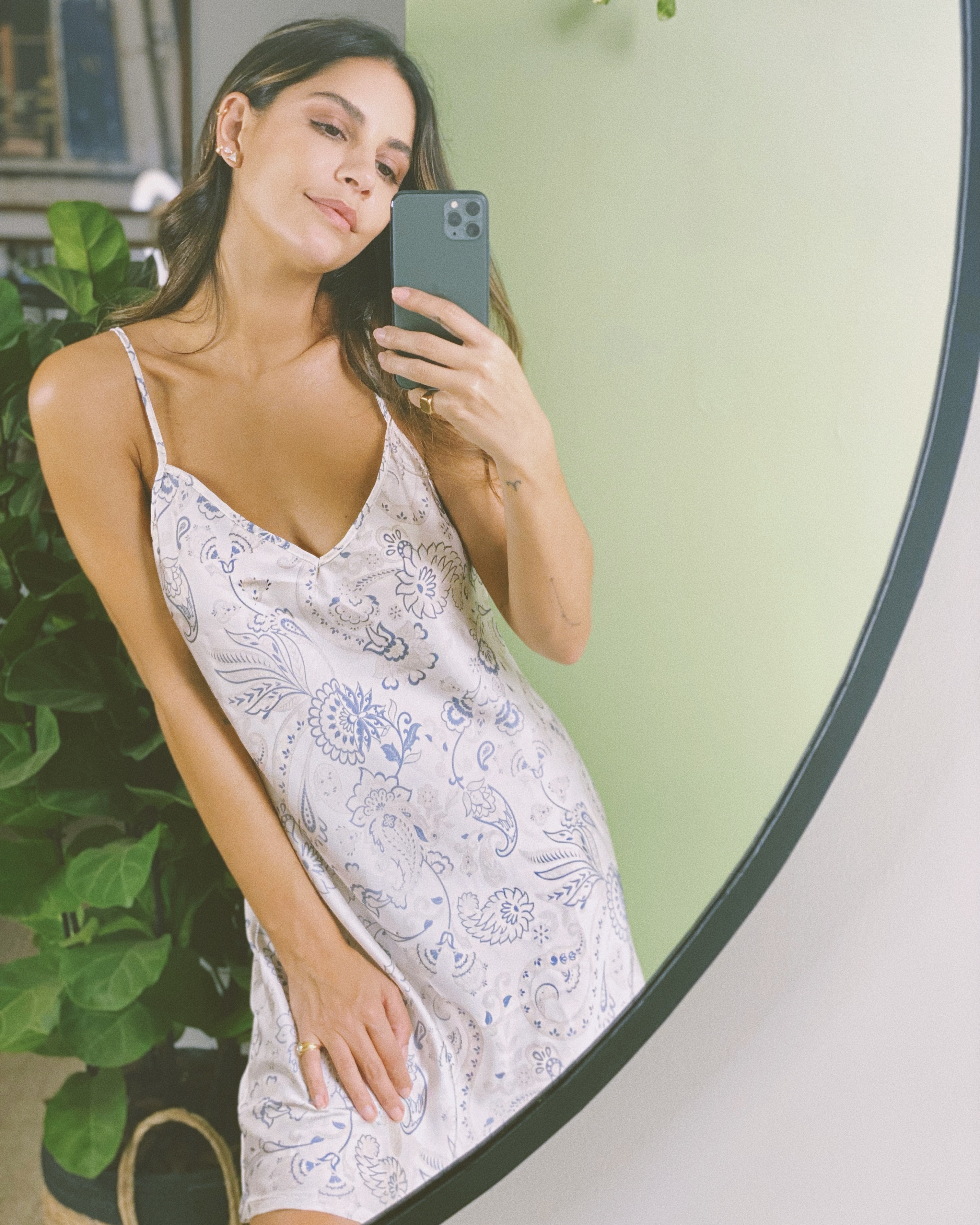 Mulher veste camisola de cetim branco com estampa azul e tira uma foto no espelho. Essa é uma das sugestões de looks de verão.
