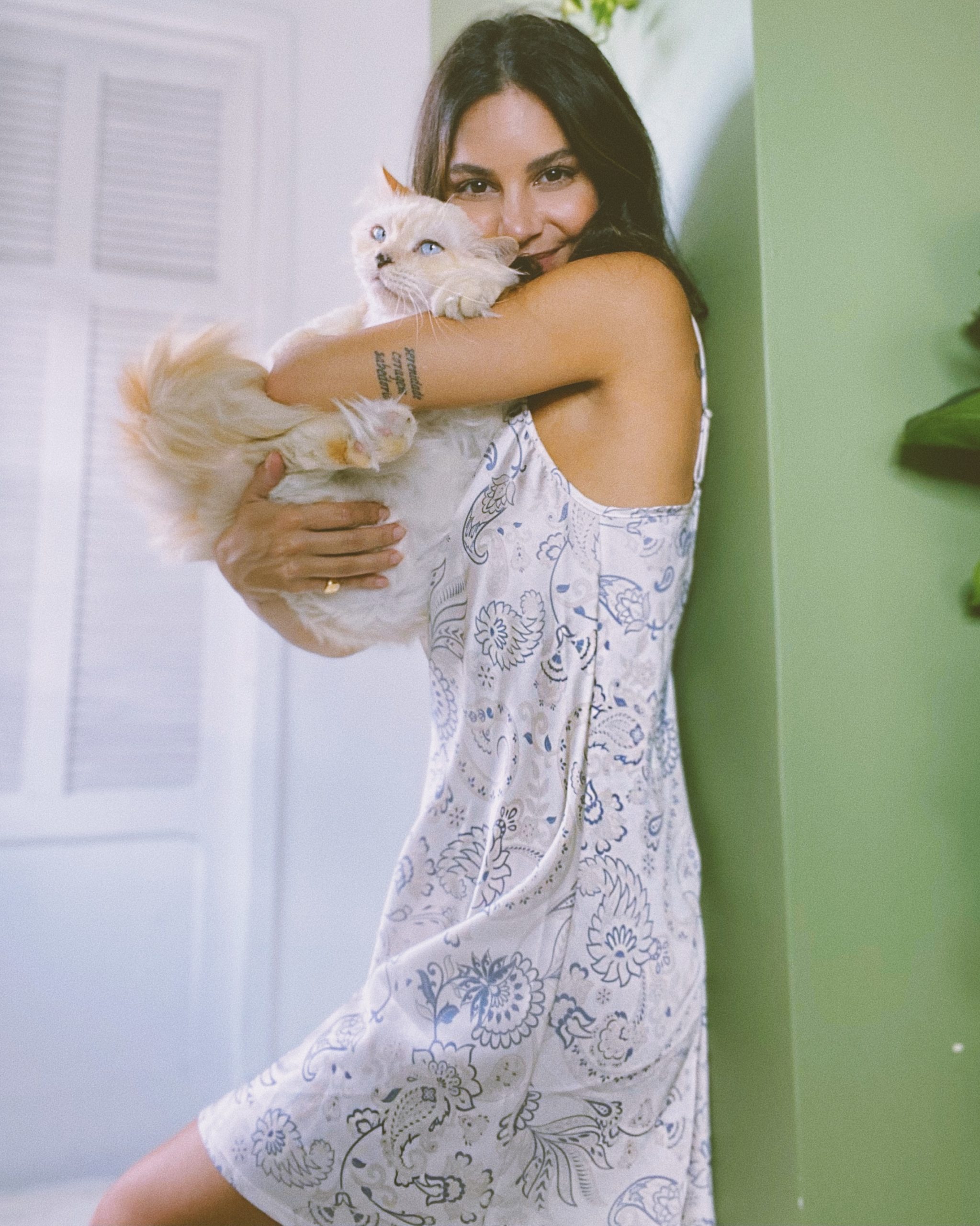 Mulher veste camisola de cetim branco com estampa azul e segura um gato. Essa é uma das sugestões de looks de verão.